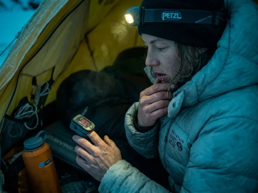 Female climber checking oxygen levels in tent at high camp