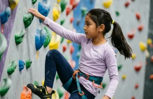 12 Indoor Climbing Games for Kids That Teach Technique Young girl placing her foot precisely on a climbing hold during an indoor kids climbing game