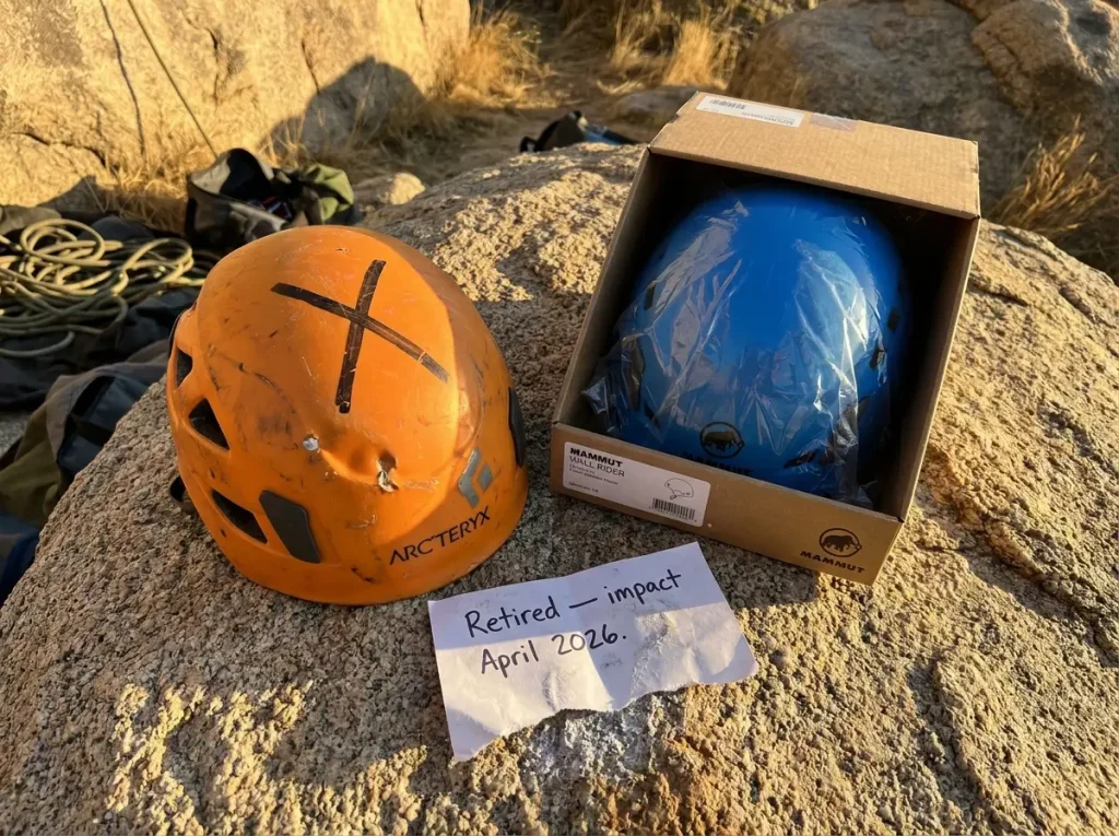 Retired climbing helmet with marker X drawn across shell sitting beside a replacement helmet at a crag