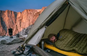 Why Sleep Is the Climbing Training You Skip Most Climber sleeping in tent at base of granite crag with climbing gear laid out beside them