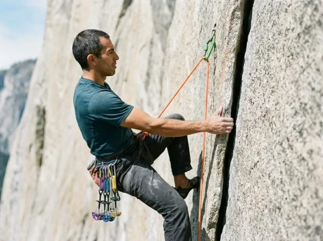 trad-climbing-grade-conversion-chart-hero Trad climber laybacking a granite crack with Black Diamond Camalot placed above on a sunlit cliff face