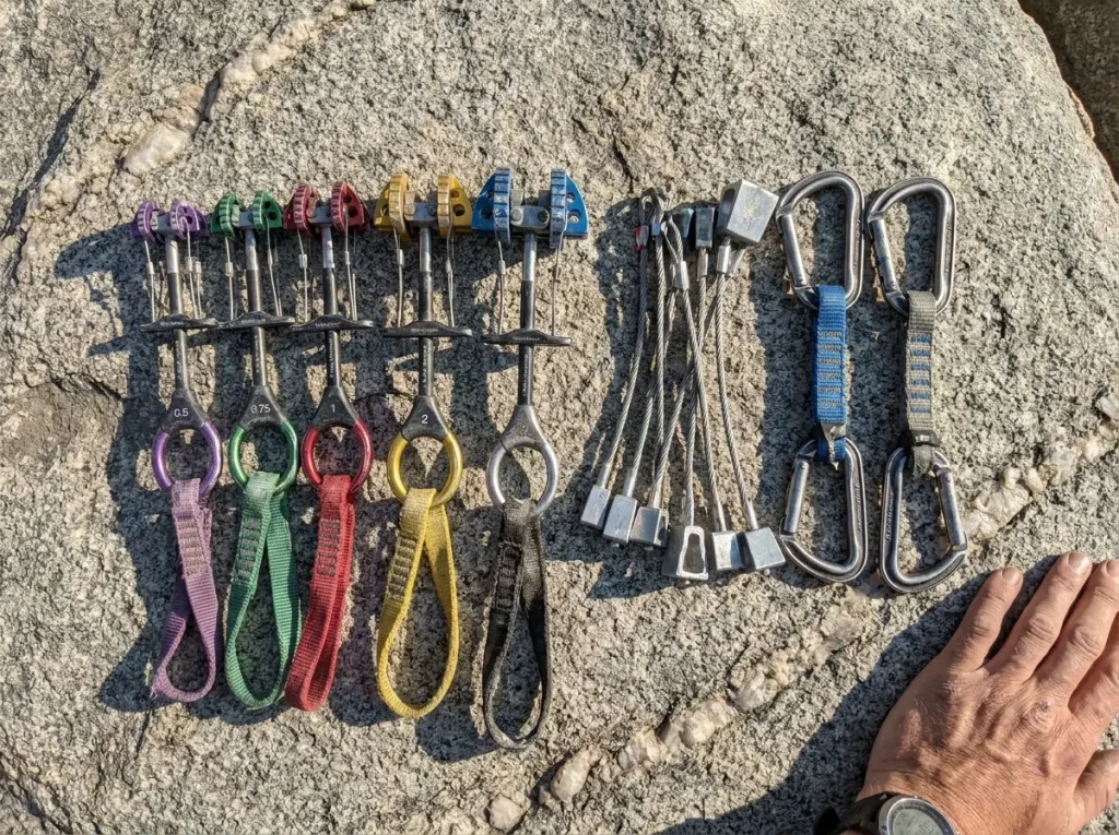 Used Black Diamond trad rack with cams and carabiners laid out for inspection on granite
