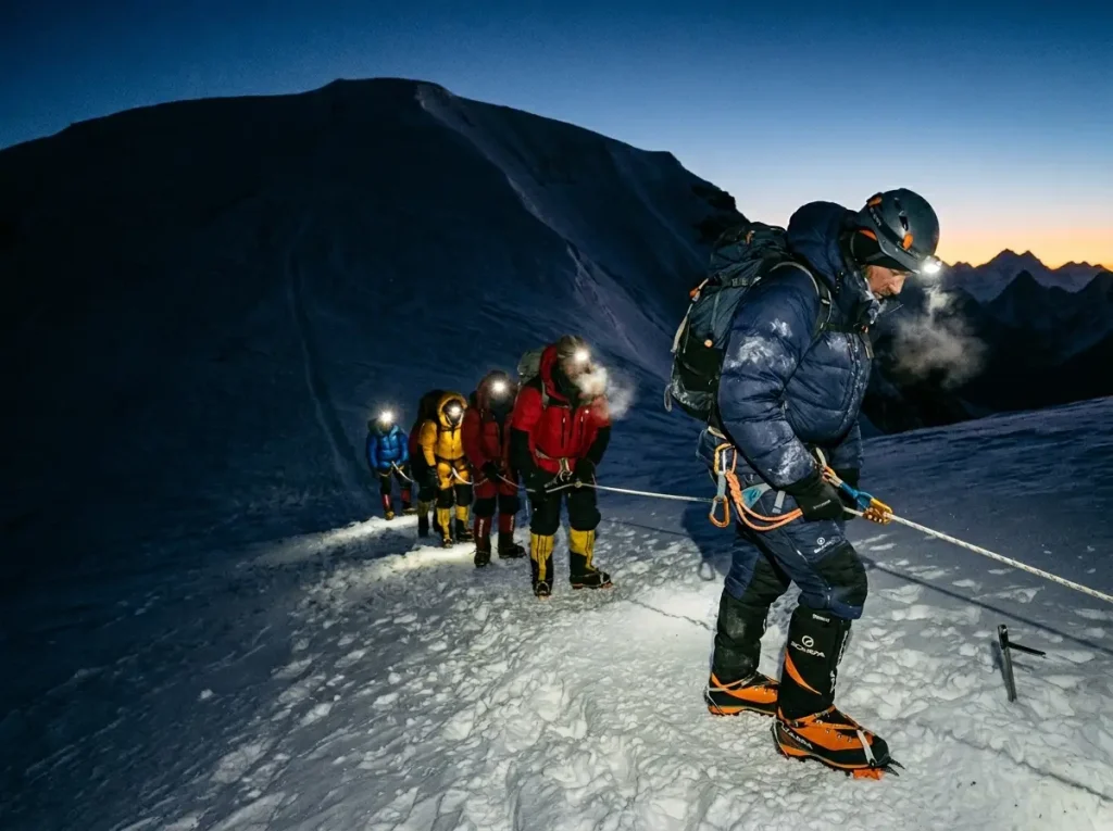 A line of climbers on a fixed rope at dawn showing crowding on a famous peak