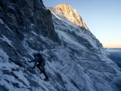 40 Eiger North Face Routes and the One to Know Roped climber small against the vast Eiger North Face at first light