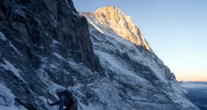 40 Eiger North Face Routes and the One to Know Roped climber small against the vast Eiger North Face at first light