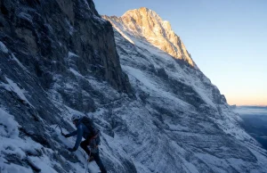 40 Eiger North Face Routes and the One to Know Roped climber small against the vast Eiger North Face at first light