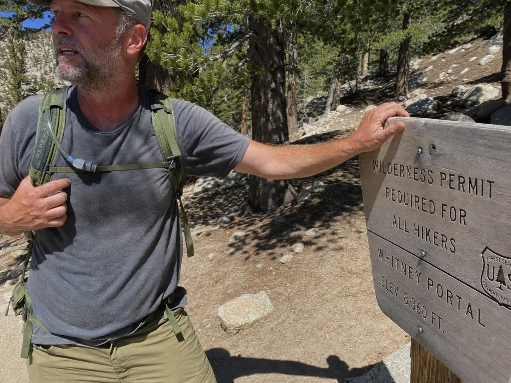 Hiker checking the Whitney Portal trailhead sign at the start of the Mount Whitney Trail