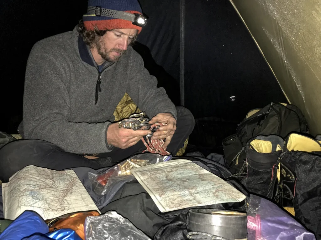 Climber sorting expedition gear inside a Base Camp tent at dusk during a weather wait