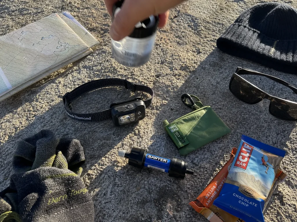 Mount Whitney essential gear laid out on granite including a Black Diamond Spot 400 headlamp and merino socks