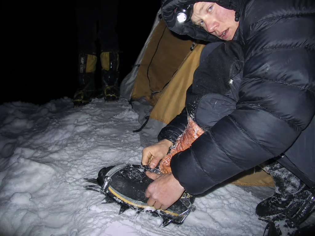 Climber checking crampon straps by headlamp before a Mount Rainier alpine start