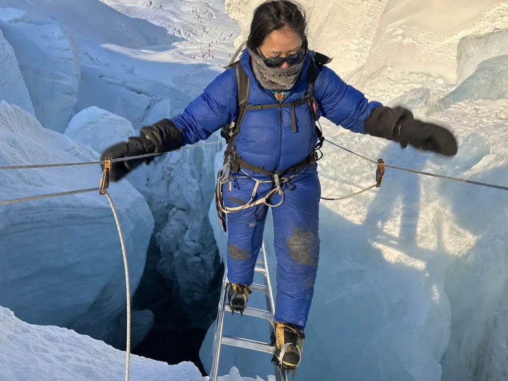 Climber crossing a ladder over a crevasse in the Khumbu Icefall on the South Col route