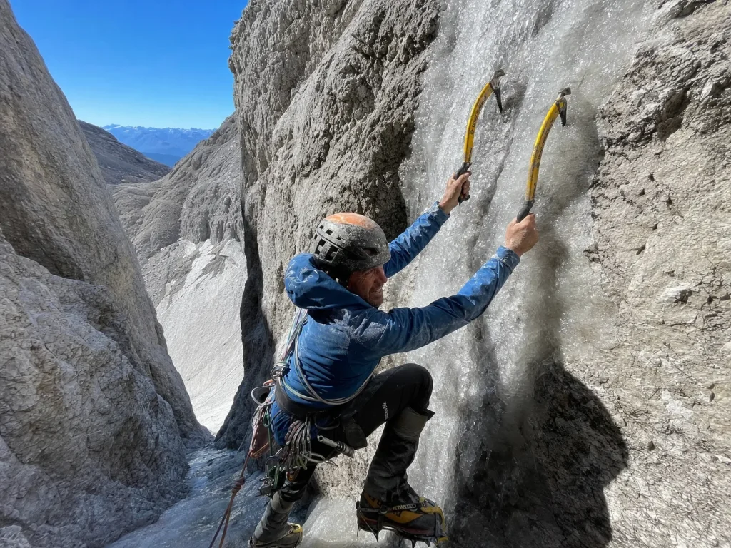 Alpinist front-pointing up a steep grey ice runnel on the Eiger with two ice tools