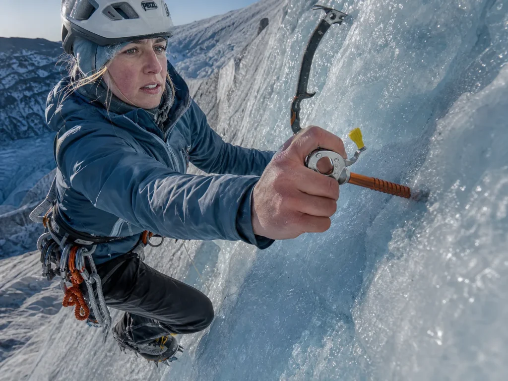 Climber placing a Petzl ice screw on a steep ice slope of Kautz Glacier