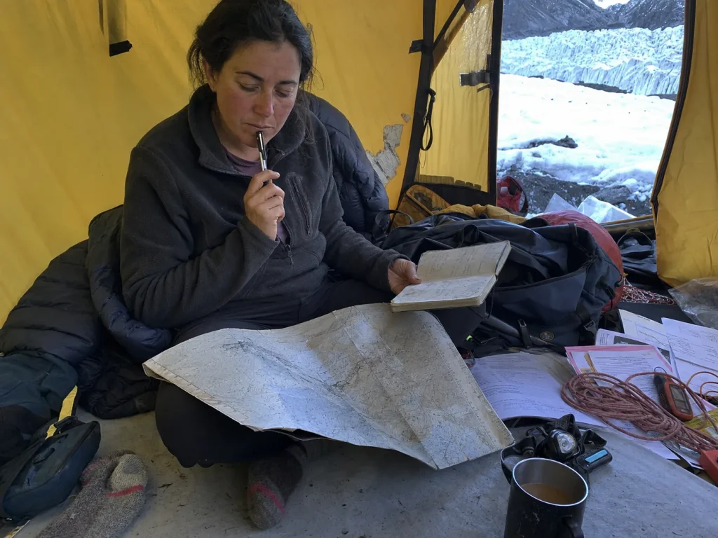 Climber weighing route choices over a map and notebook inside an expedition tent