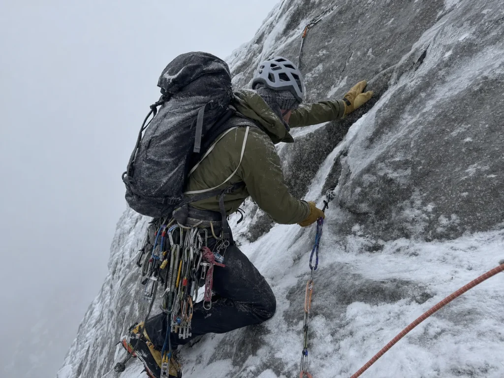 Climber leading iced-up mixed rock on the Eiger with a heavy pack and full rack