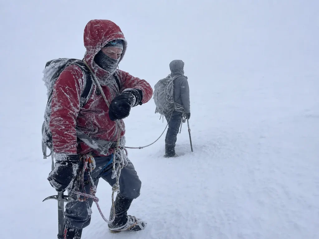 Roped climbers pausing in a whiteout to decide whether to turn back on Mount Rainier
