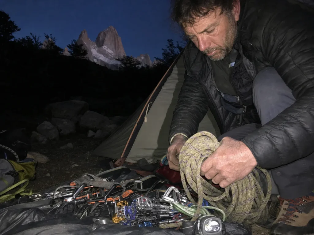 Climber sorting glacier gear at Poincenot base camp below Fitz Roy at dusk