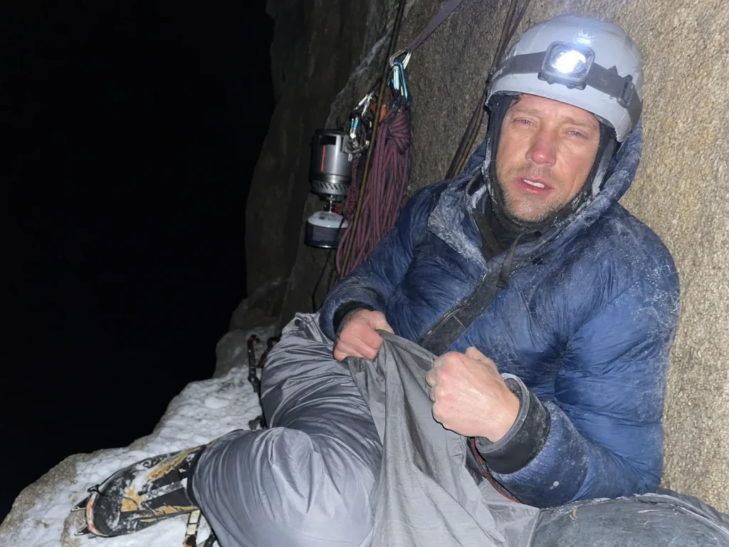 Climber lashed to an anchor for a forced bivouac on a narrow Eiger ledge at dusk