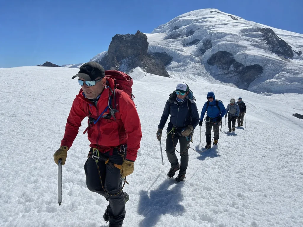 A guided rope team following a lead guide up a snow slope on Mount Rainier