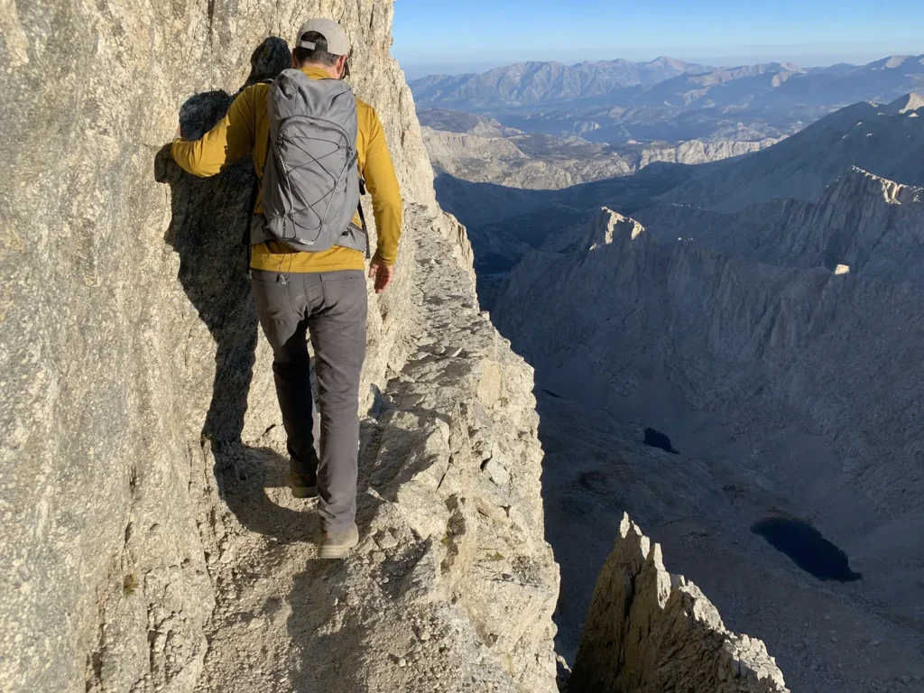 Hiker on the exposed cliff-cut trail just past Trail Crest on Mount Whitney