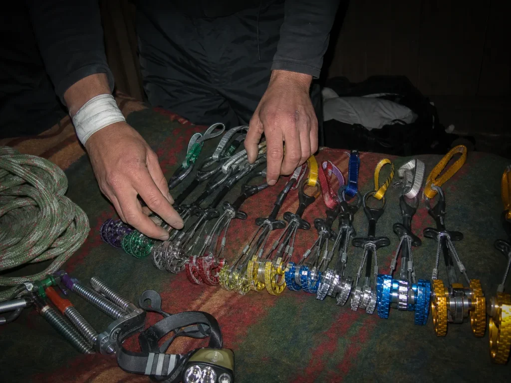 Climber laying out a Black Diamond Camalot C4 rack on a hostel bunk at dusk before a Cerro Torre attempt