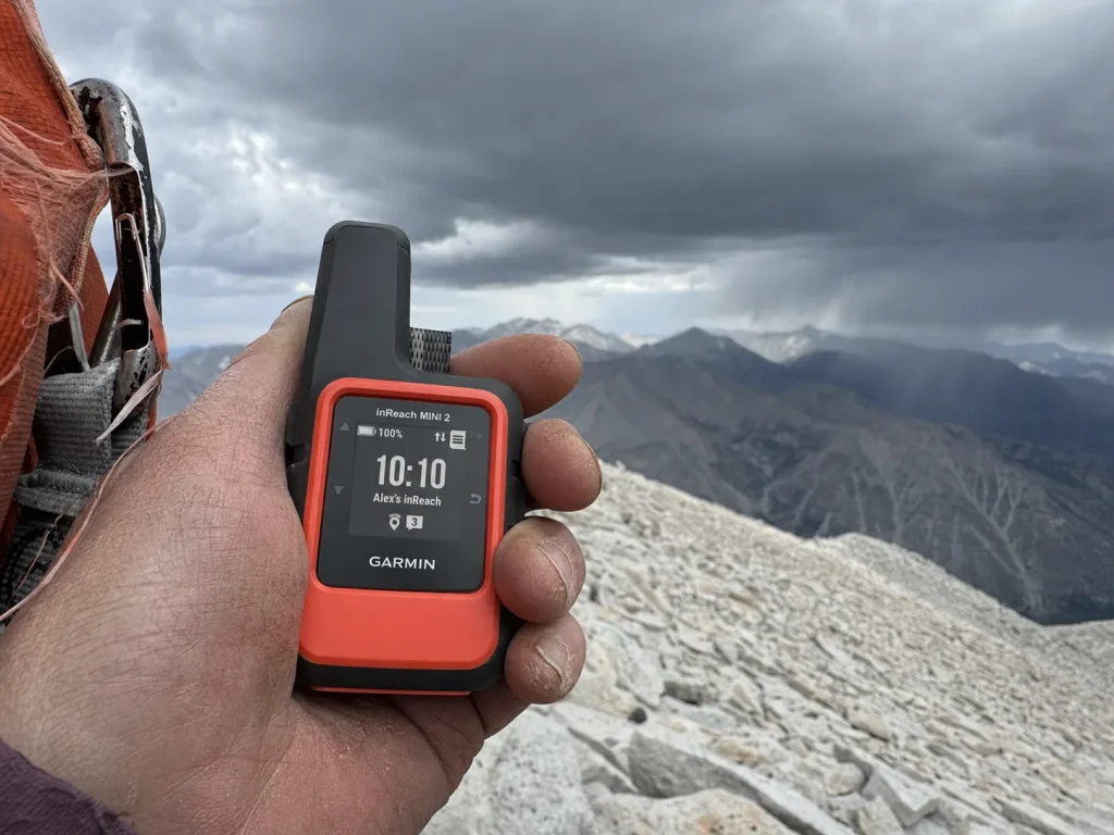 Garmin inReach Mini 2 satellite communicator held above treeline as afternoon storm clouds build