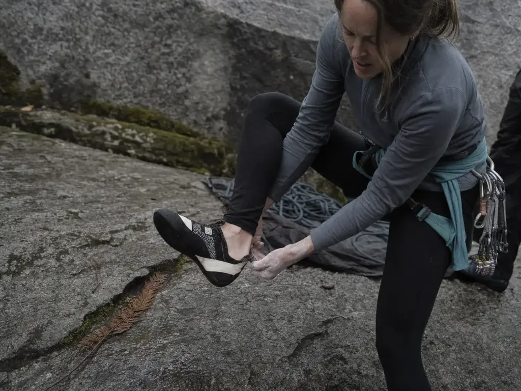 Woman climber pulling on a low-volume women's lace-up climbing shoe at a multi-pitch base
