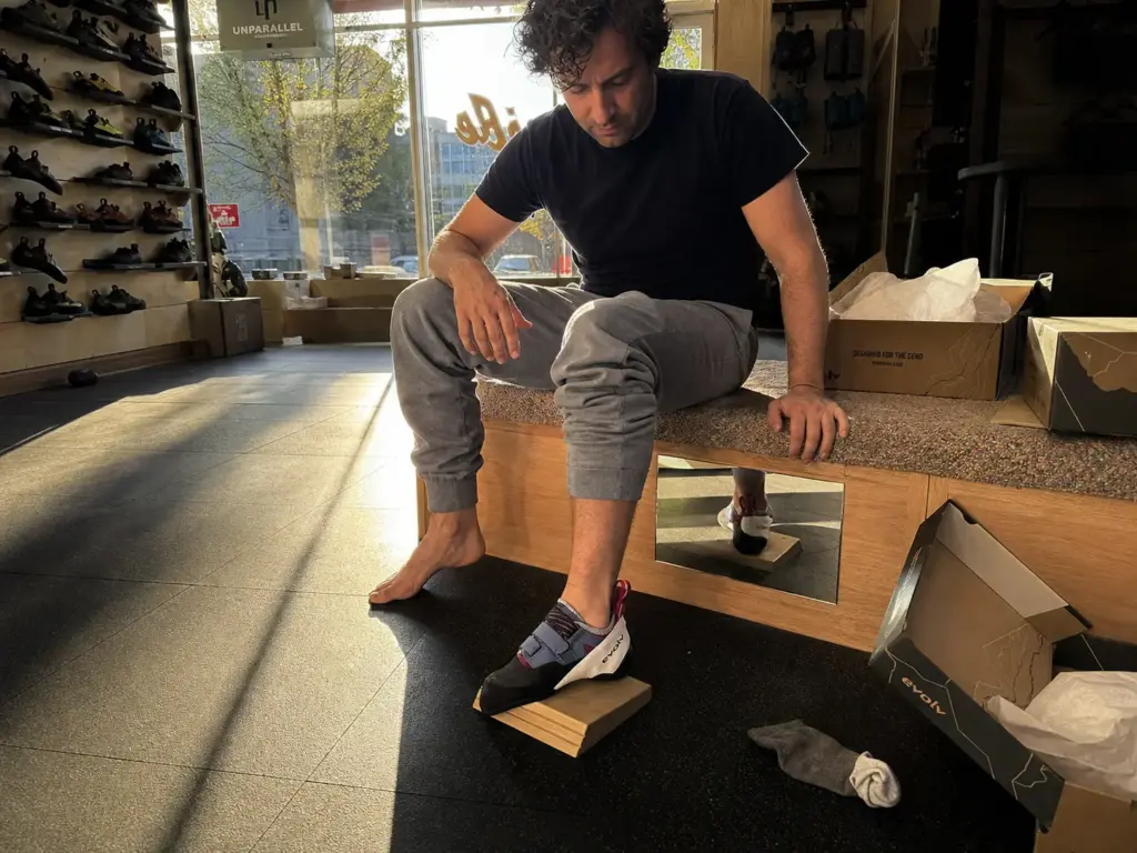 Climber testing climbing shoe fit late in the day when feet have swollen at a gear shop bench