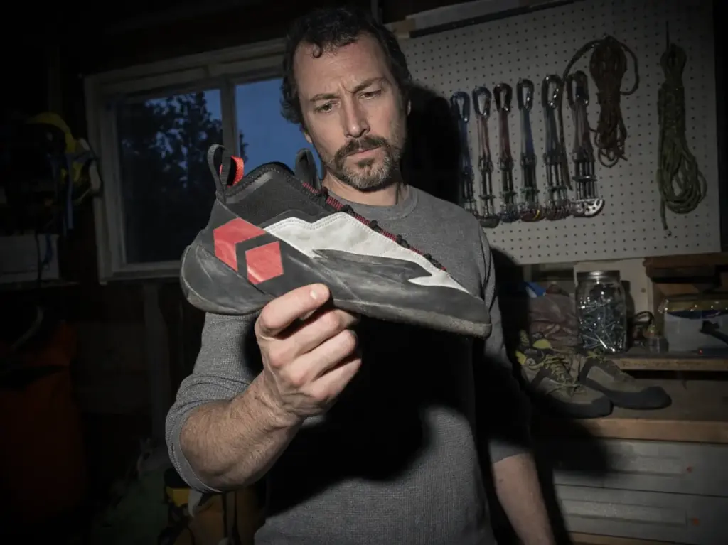 Climber inspecting the worn toe rubber and scuffed side rand of a low-top trad climbing shoe
