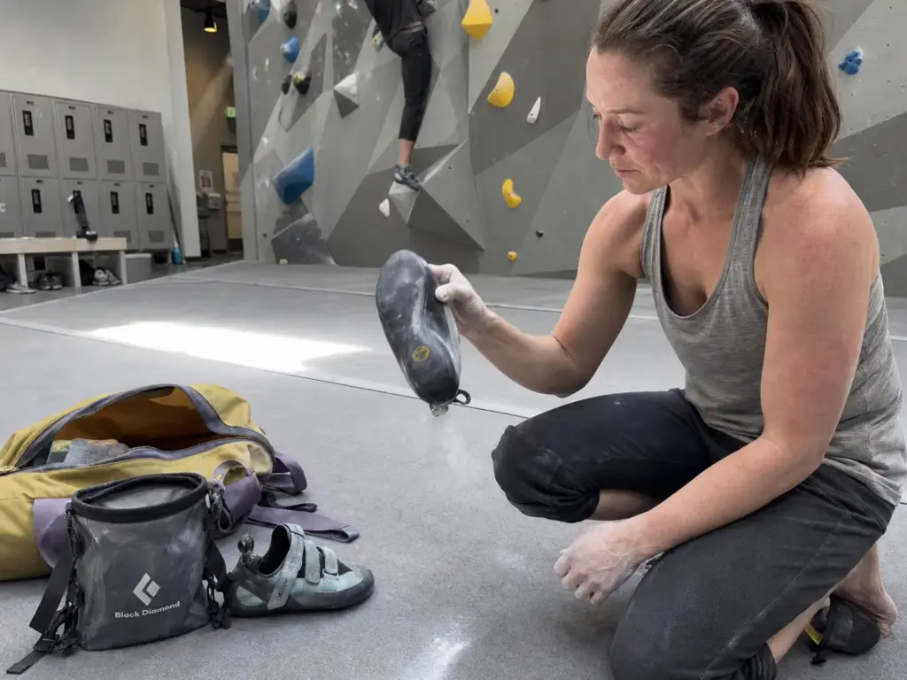 Climber airing out climbing shoes and knocking chalk out at the base of a gym wall