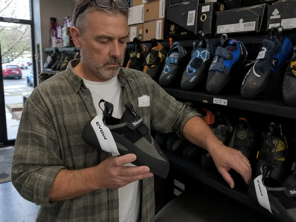 Climber comparing wide-fitting climbing shoes from several brands on a shop shelf